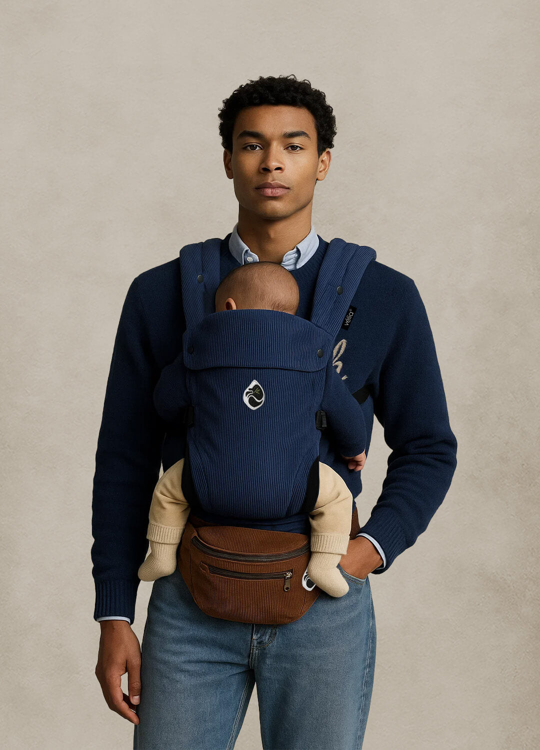 Model trägt die Velia Nuvola Cord Babytrage in Bleu Nord mit Essenza Bag in Braun – stilvoller Kontrast aus kühlem Blau und warmem Naturton.