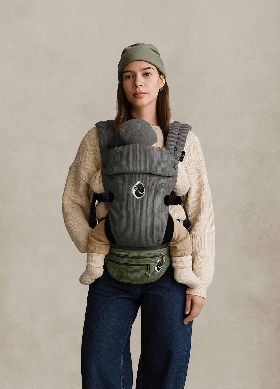 Model trägt die Velia Nuvola Cord Babytrage in Gris Lune mit Essenza Bag in Hellgrün – High-Fashion Look mit ergonomischem Design für modernen Alltag.